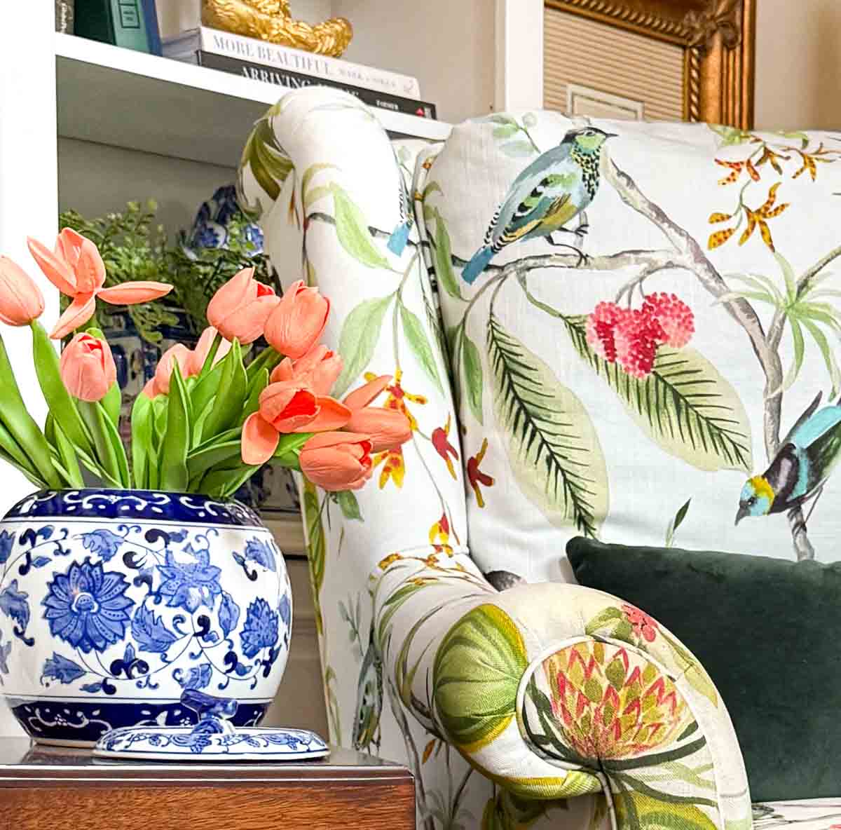 coral tulips in a blue and white container on a small wood table beside a colorful traditional arm chair for spring