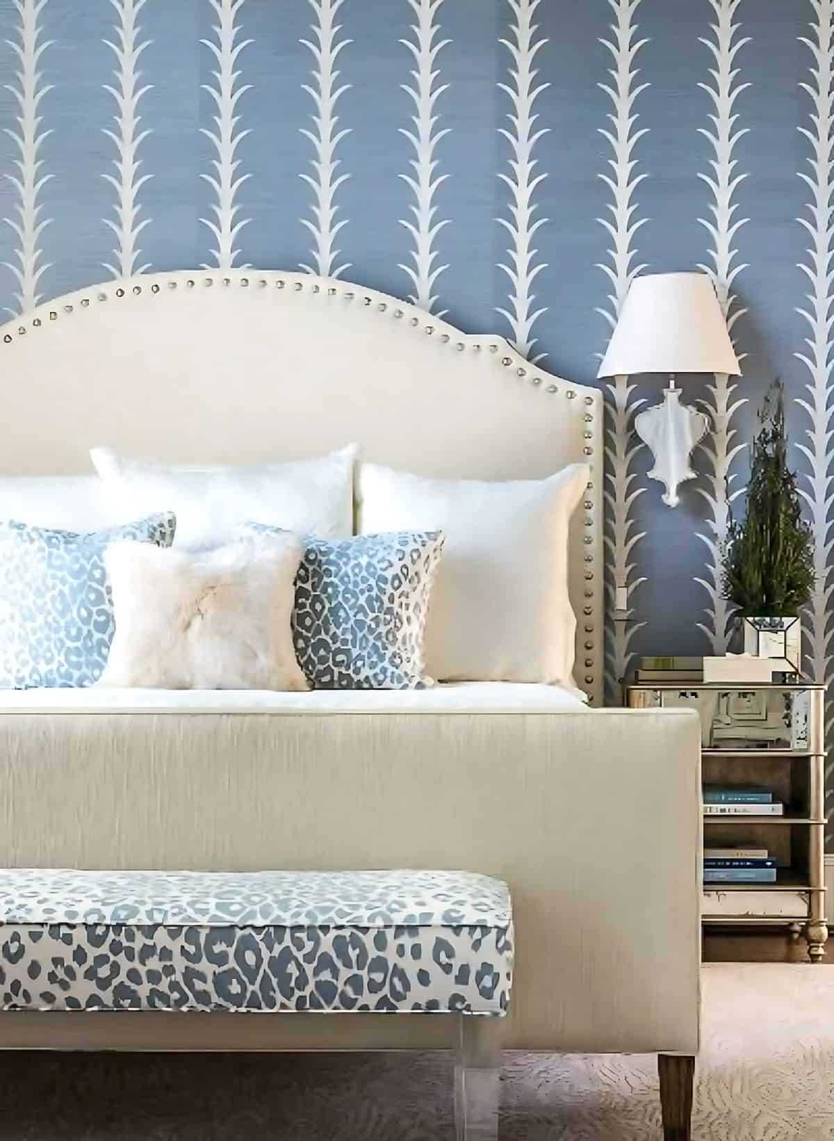 neutral upholstered bed in front of a blue patterned wallpapered wall