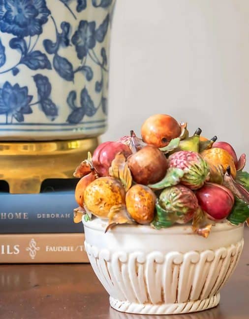 small Italian ceramic bowl of mixed fruit in front on a blue and white lamp on a wooden table