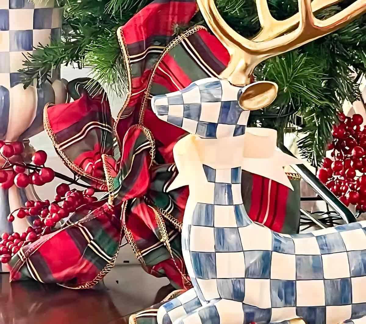 blue and white sitting deer in front of a red plaid Christmas bow