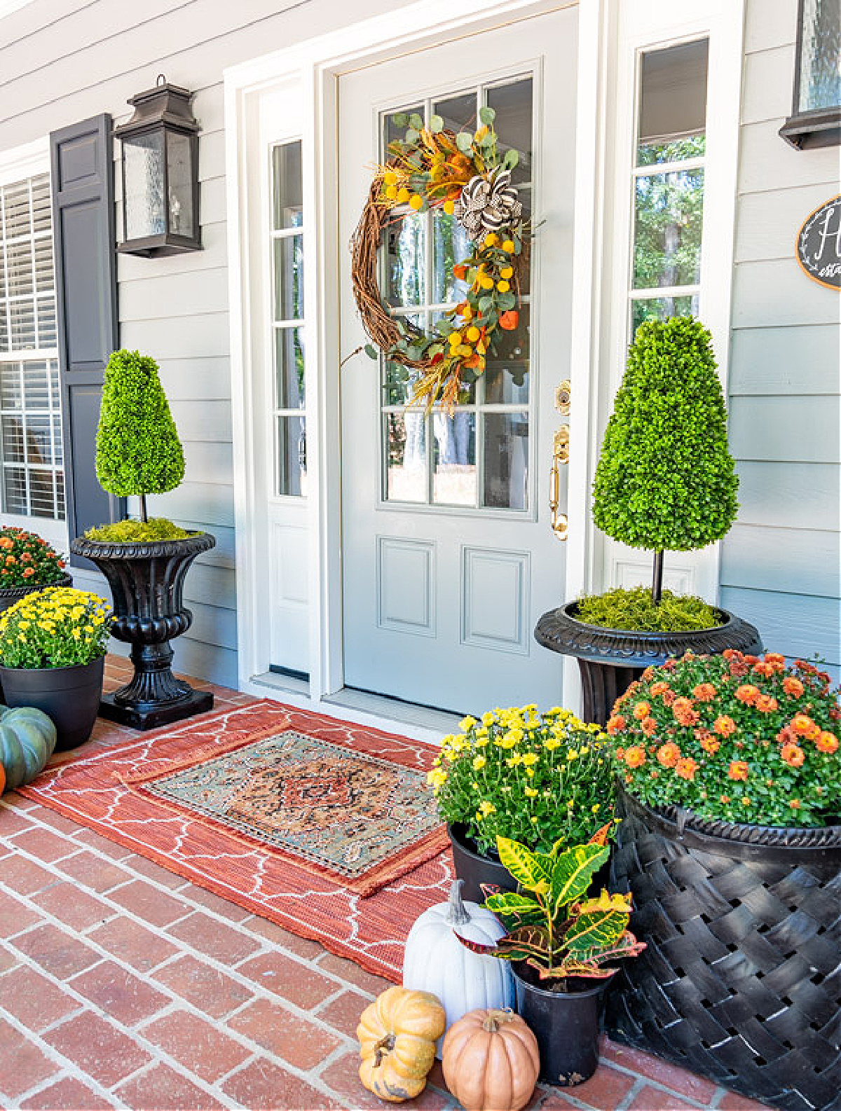 front porch with a gray front door with fall wreath and other fall decor in traditional fall colors