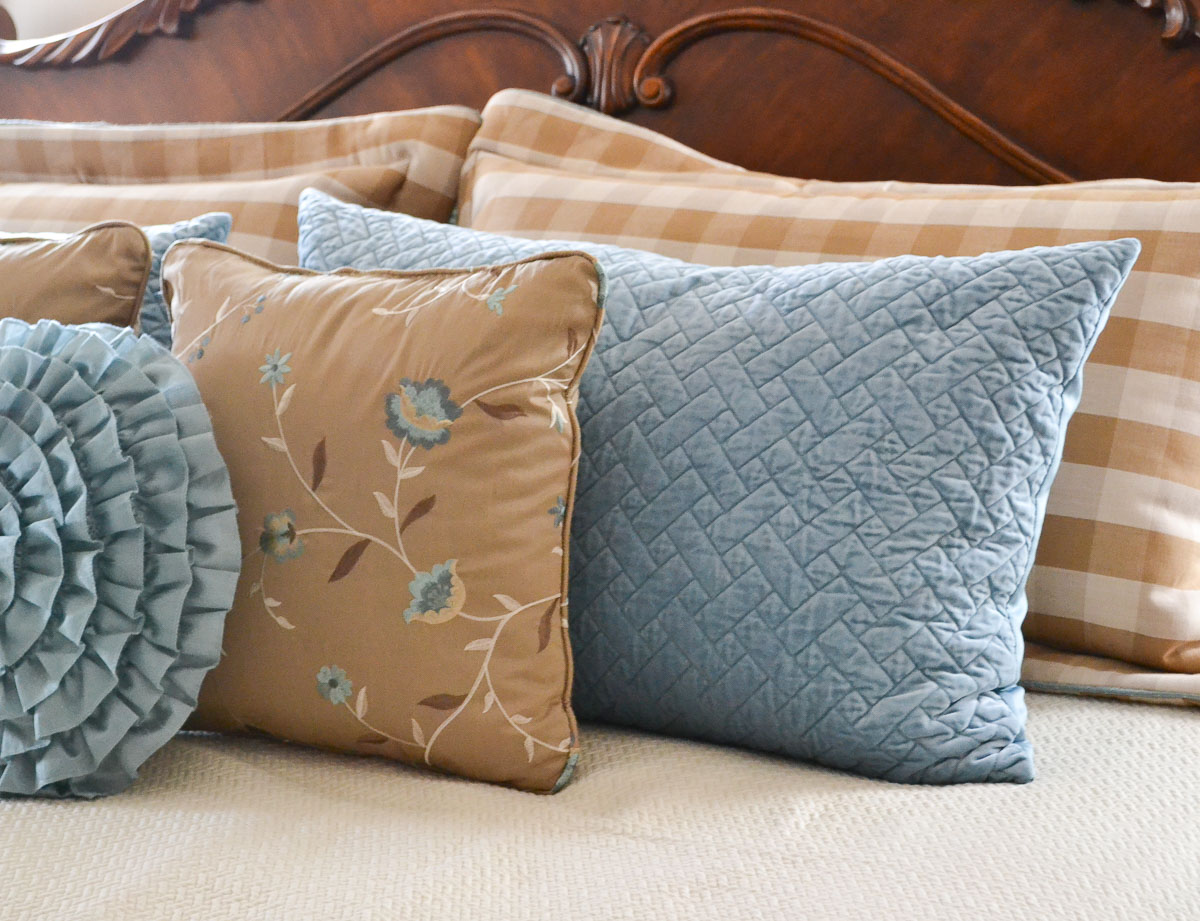 brown and tan pillow shams mixed with blue pillow shams and throw pillows leaning against a wood headboard