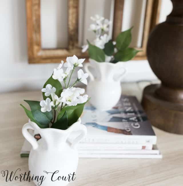 white home decor accessories filled with faux white flowers on a nightstand