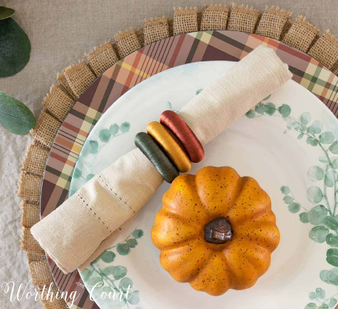 Thanksgiving tablescape with faux orange pumpkins, green eucalyptus and neutral linens