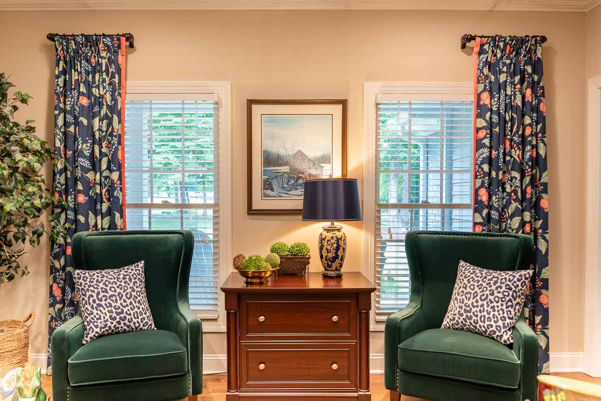 pair of green velvet chairs positioned in front of window with navy blue floral draperies
