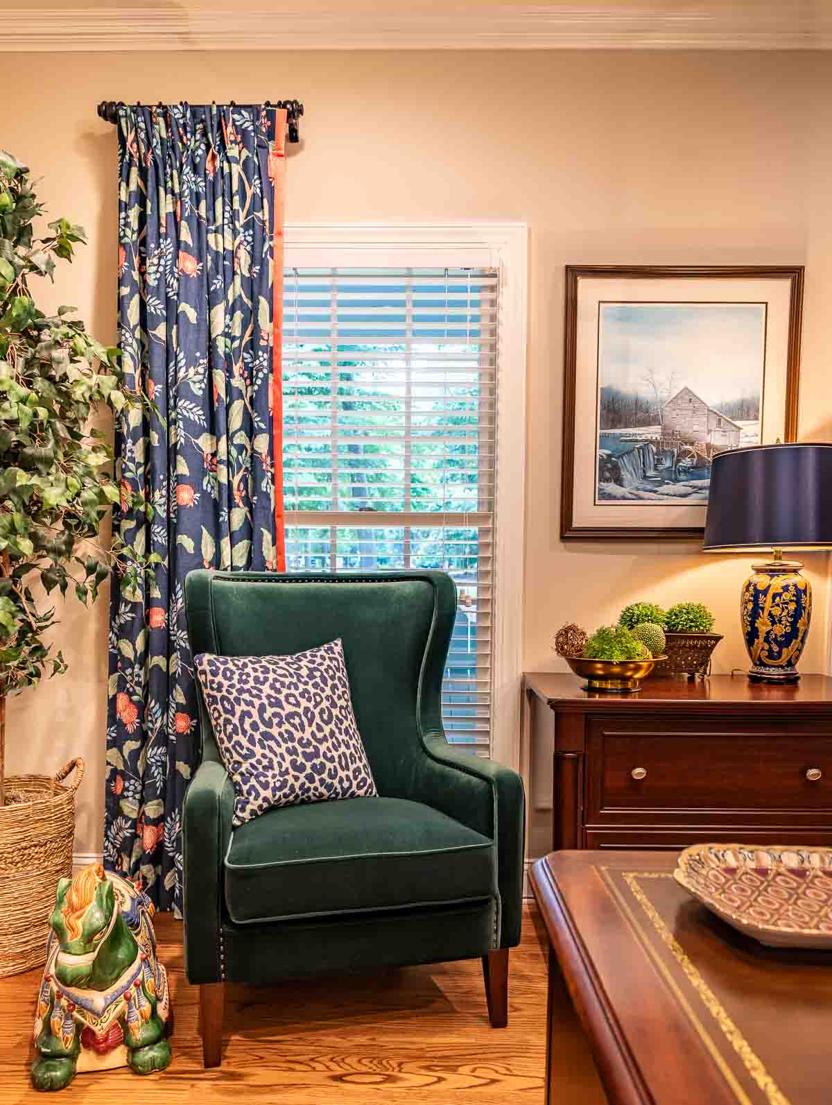 green velvet chair positioned in front of window with navy blue floral draperies