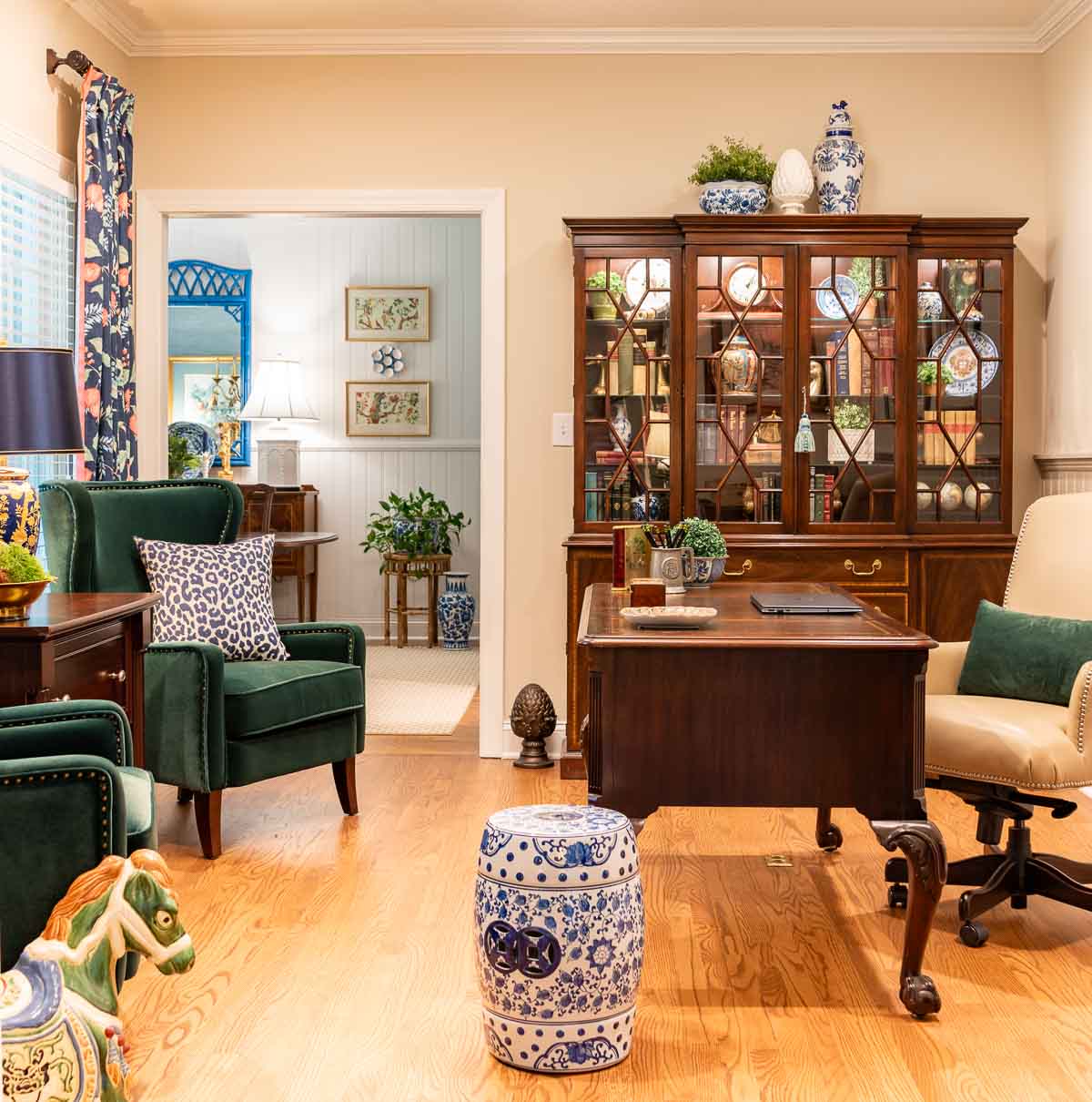 home office with traditional wood furniture, green velvet arm chairs, navy blue floral curtains and colorful accessories