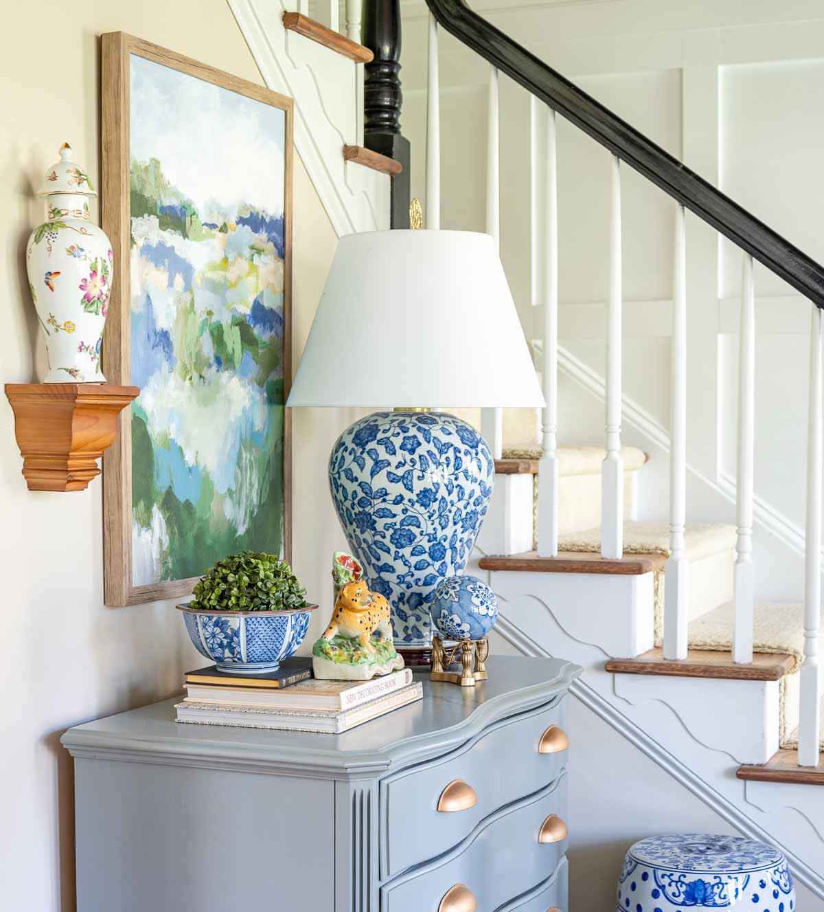small gray chest beside a staircase in a foyer decorated with chinoiserie accessories and abstract artwork