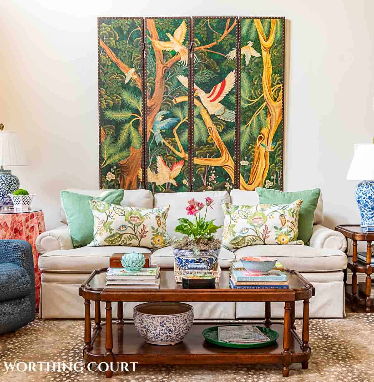 coffee table in front of tan couch with chinese screen on the wall and late summer chinoiserie accessories