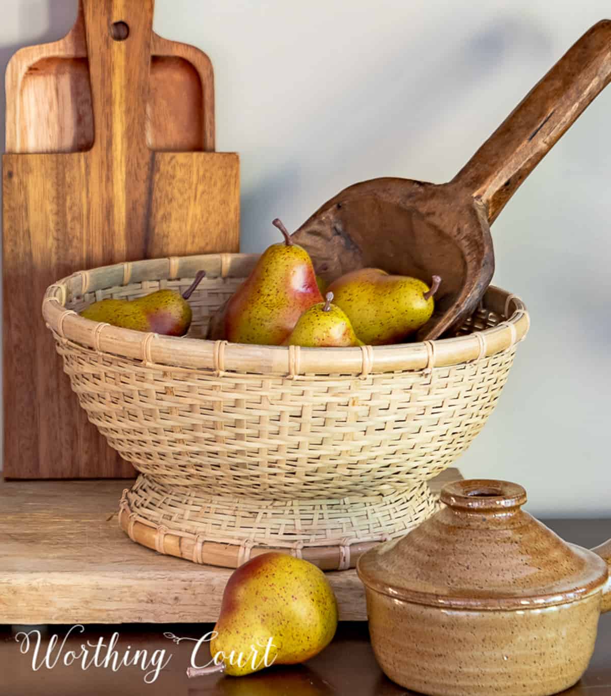 wood scoop in a wicker bowl filled with faux mini pears on a wood cutting board