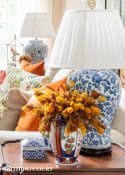 blue and white lamp and a vase filled with fall stems on a brown wood end table