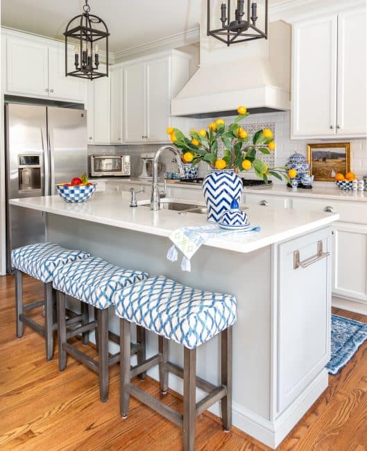 kitchen with white cabinets and a white tile backsplash and white quartz counters decorated with blue and white accessories and oranges stems in a vase