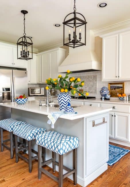 kitchen with white cabinets and a white tile backsplash and white quartz counters decorated with blue and white accessories and oranges stems in a vase