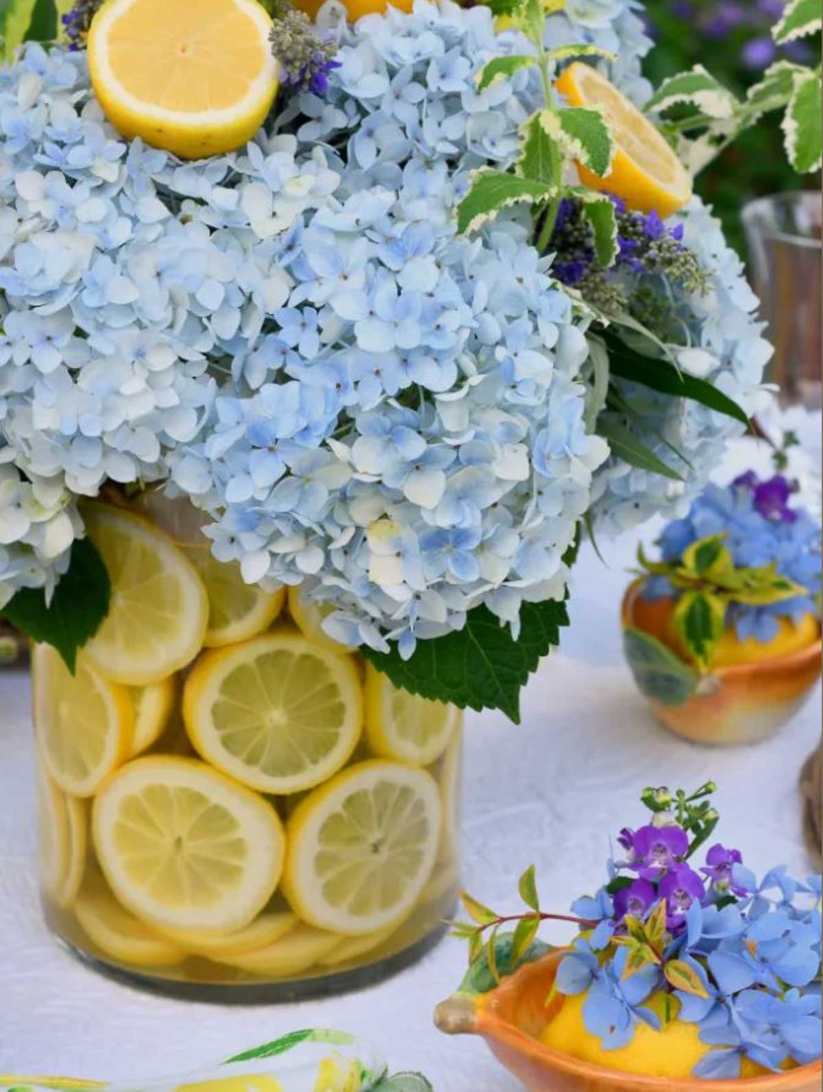 clear glass vase with sliced lemons around the side and an arrangement of blue hydrangeas