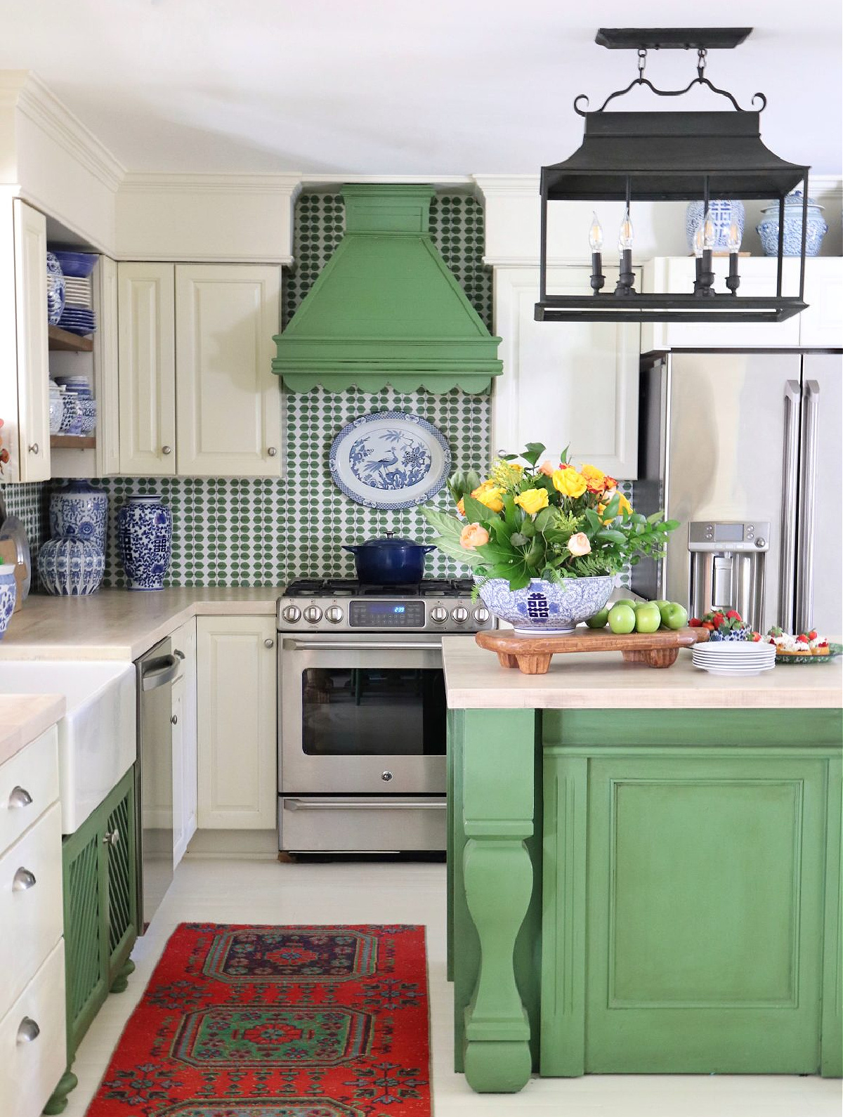 kitchen with white cabinets, a green island, a green hood with scalloped edge and green and white wallpaper backsplash