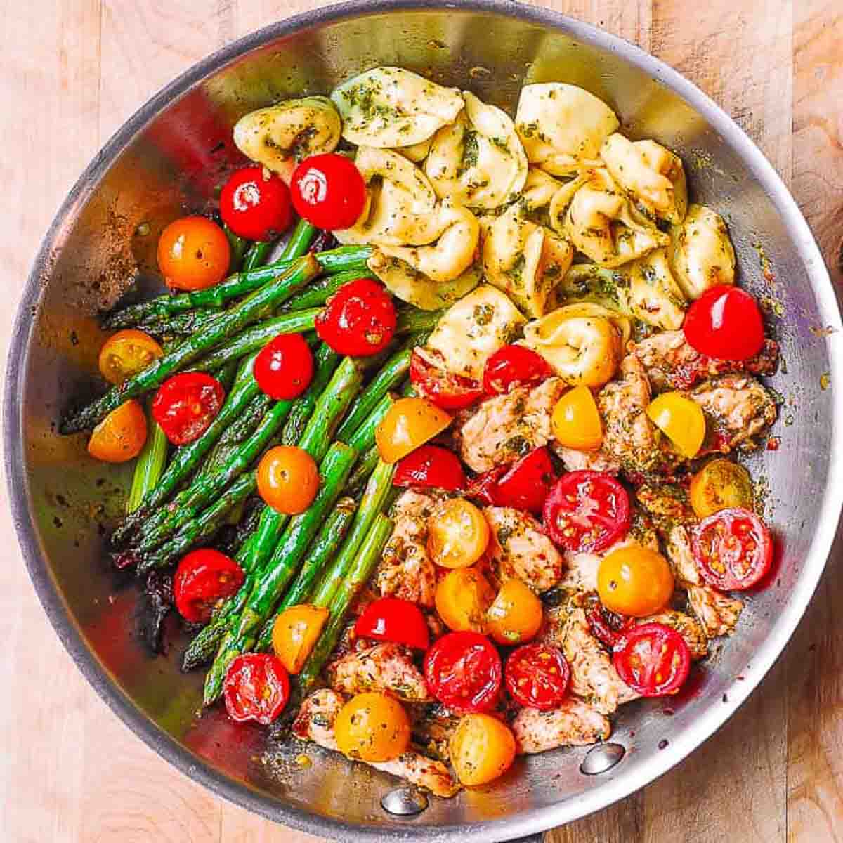 tomatoes, tortellini and asparagus in a stainless steel bowl