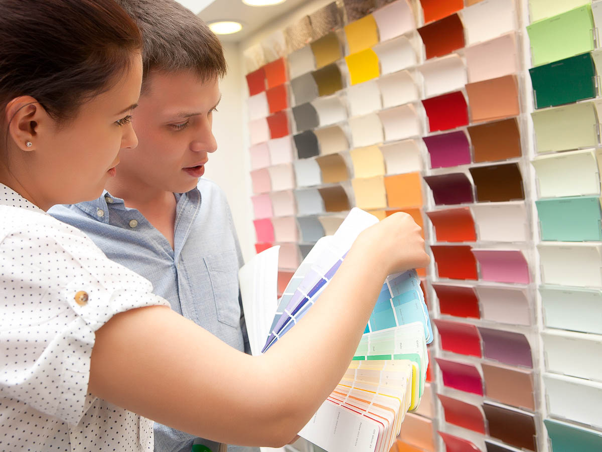 man and woman couple standing in front of a paint chip display to choose a paint color