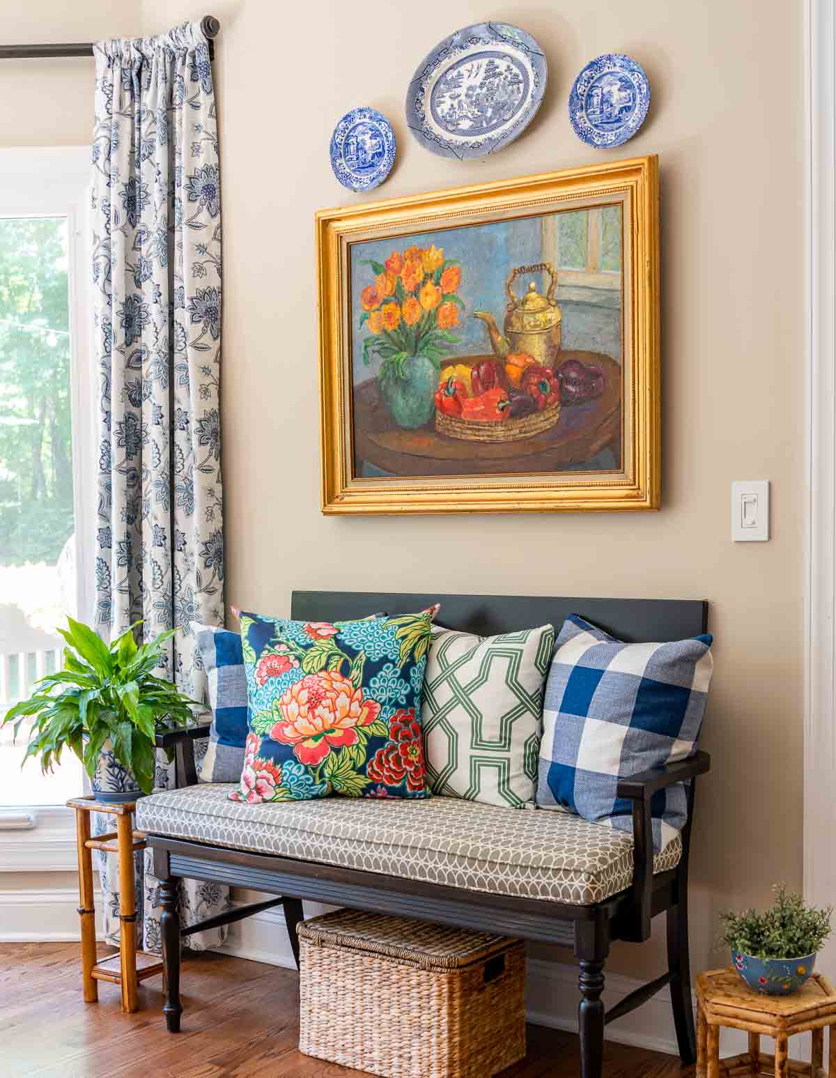 black bench with colorful summer pillows below an original oil painting