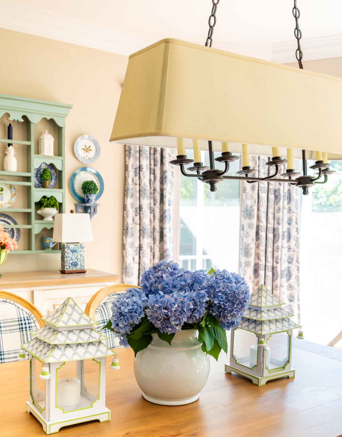 blue hydrangeas in a white vase flanked by pagoda style lanterns on a wood dining table