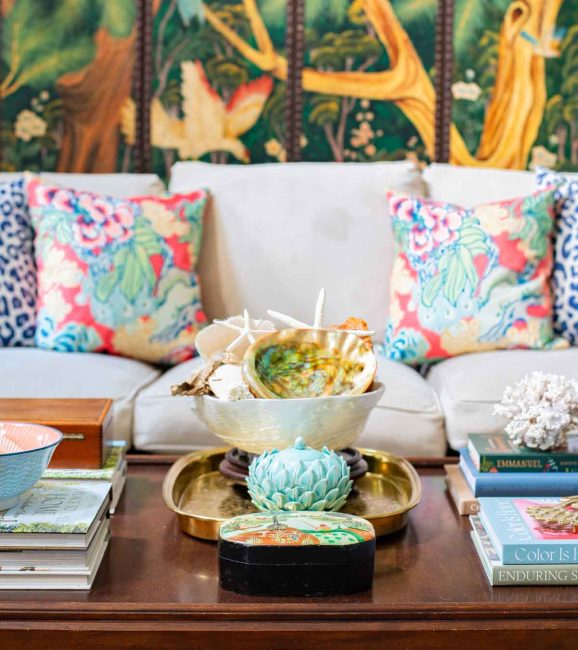 floral throw pillows on a neutral sofa with a wood coffee table in front with traditional summer accessories