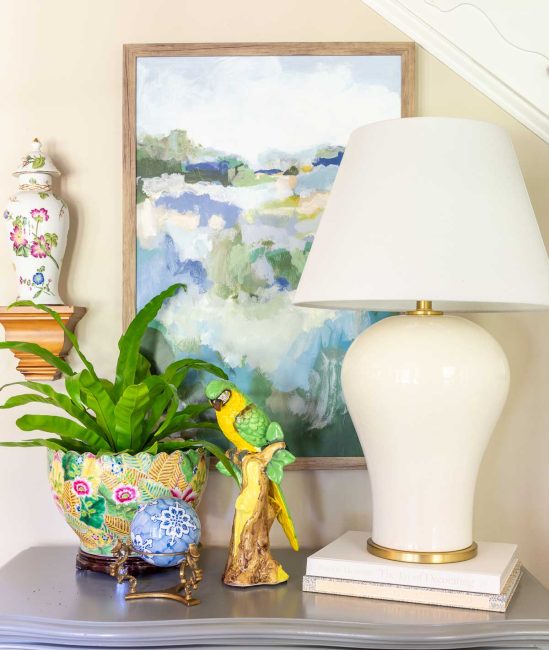 off white lamp and colorful accessories on top of a small gray chest