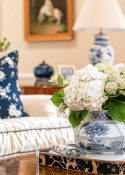 white hydrangeas in a blue and white vase on a wood coffee table in a living room with beige walls