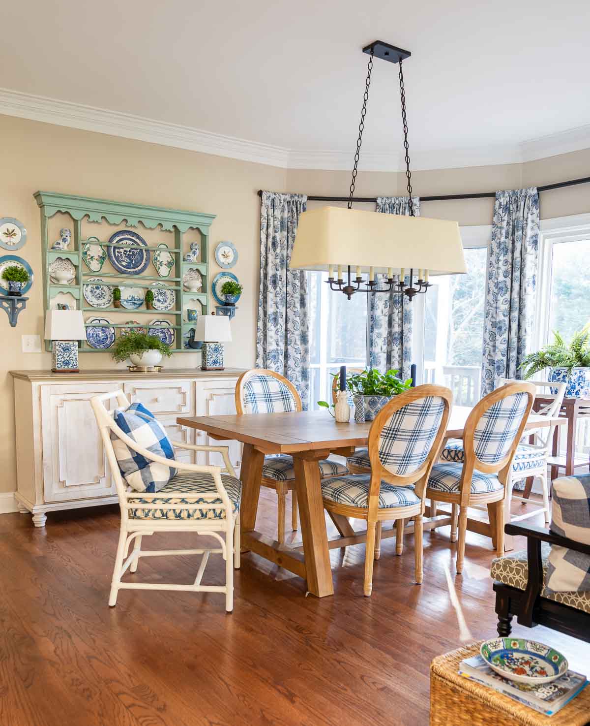 cottage style breakfast room with pine table, blue and white chairs, white sideboard with a blue plate rack above and blue and white curtains