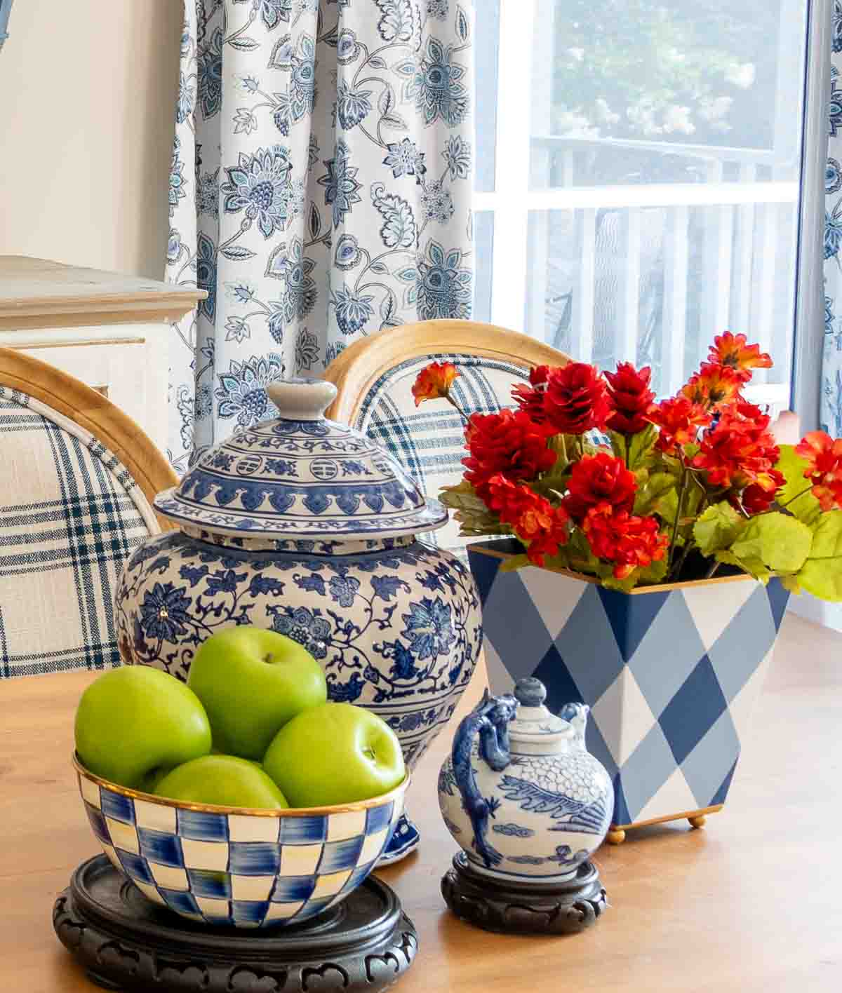 August centerpiece with blue and white accessories including a blue and white checked bowl filled with green apples and a container with fall colored flowers