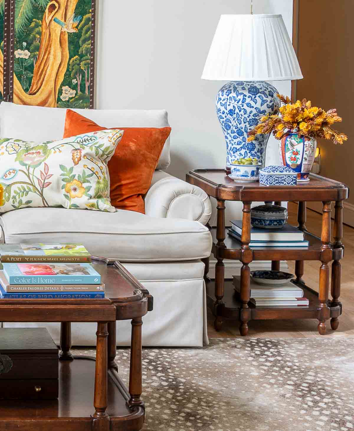 end table at the end of the couch with a blue and white lamp, one end of a coffee table and traditional style accessories and throw pillows