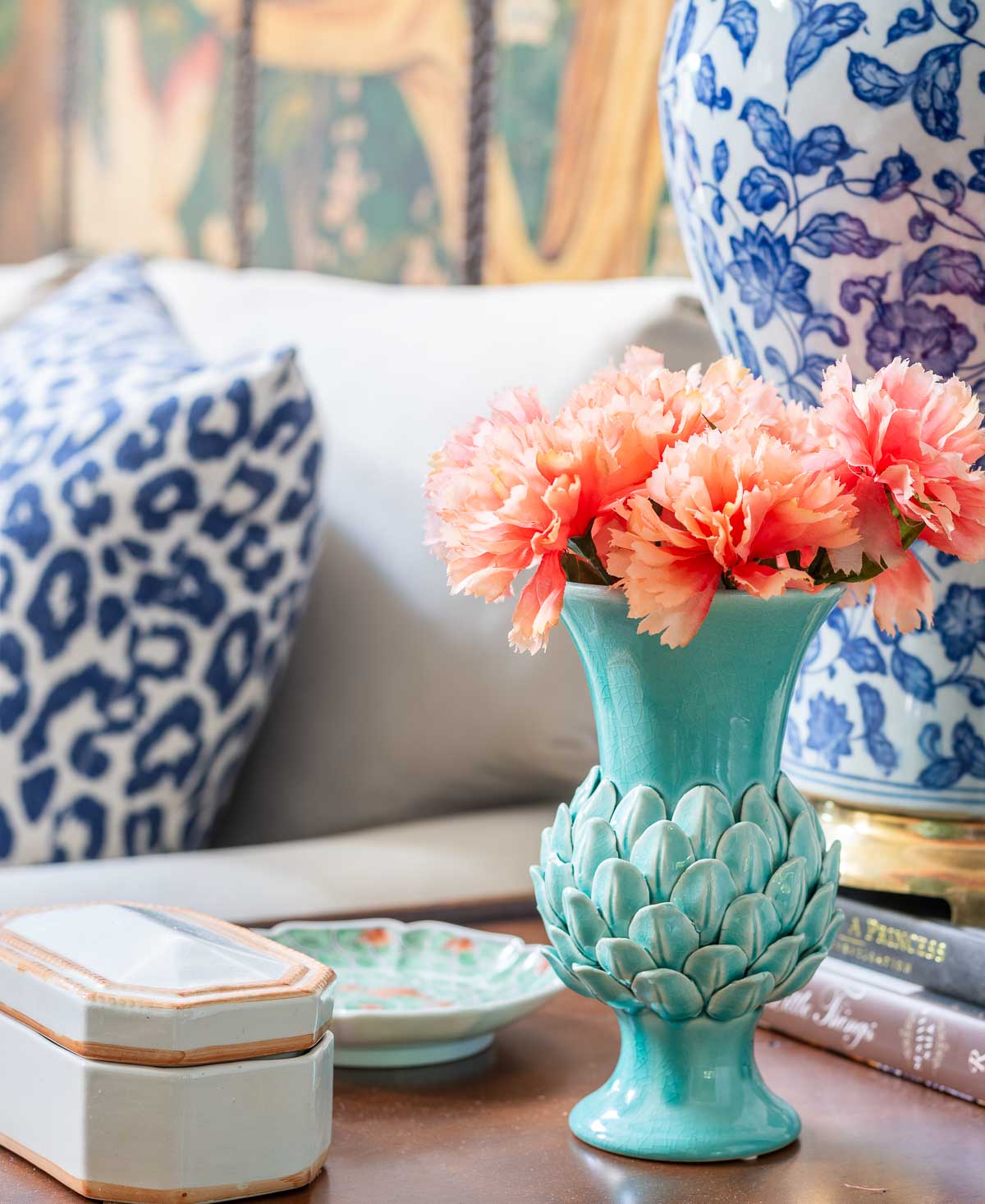 small turquoise vase of coral flowers on a wood end table beside a blue and white lamp
