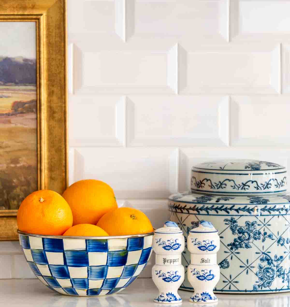 blue and white accessories and oranges in a bowl in front of a white subway tile backsplace