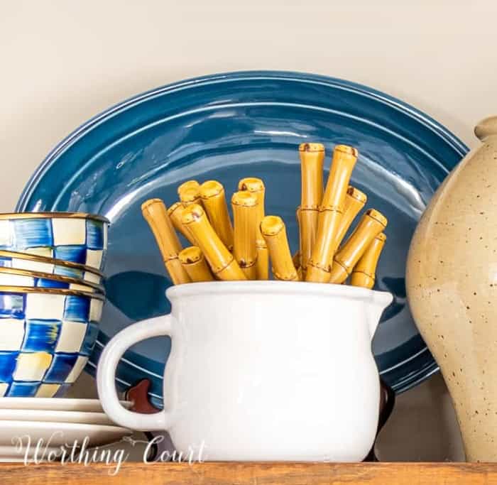 white creamer filled with bamboo handled flatware on a wood shelf with blue and white accessories