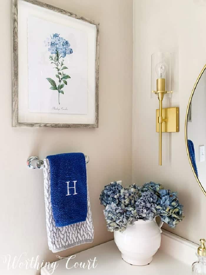 corner of a bathroom vanity with hydrangeas in a white vase, a blue hand towel and blue floral artwork on the wall