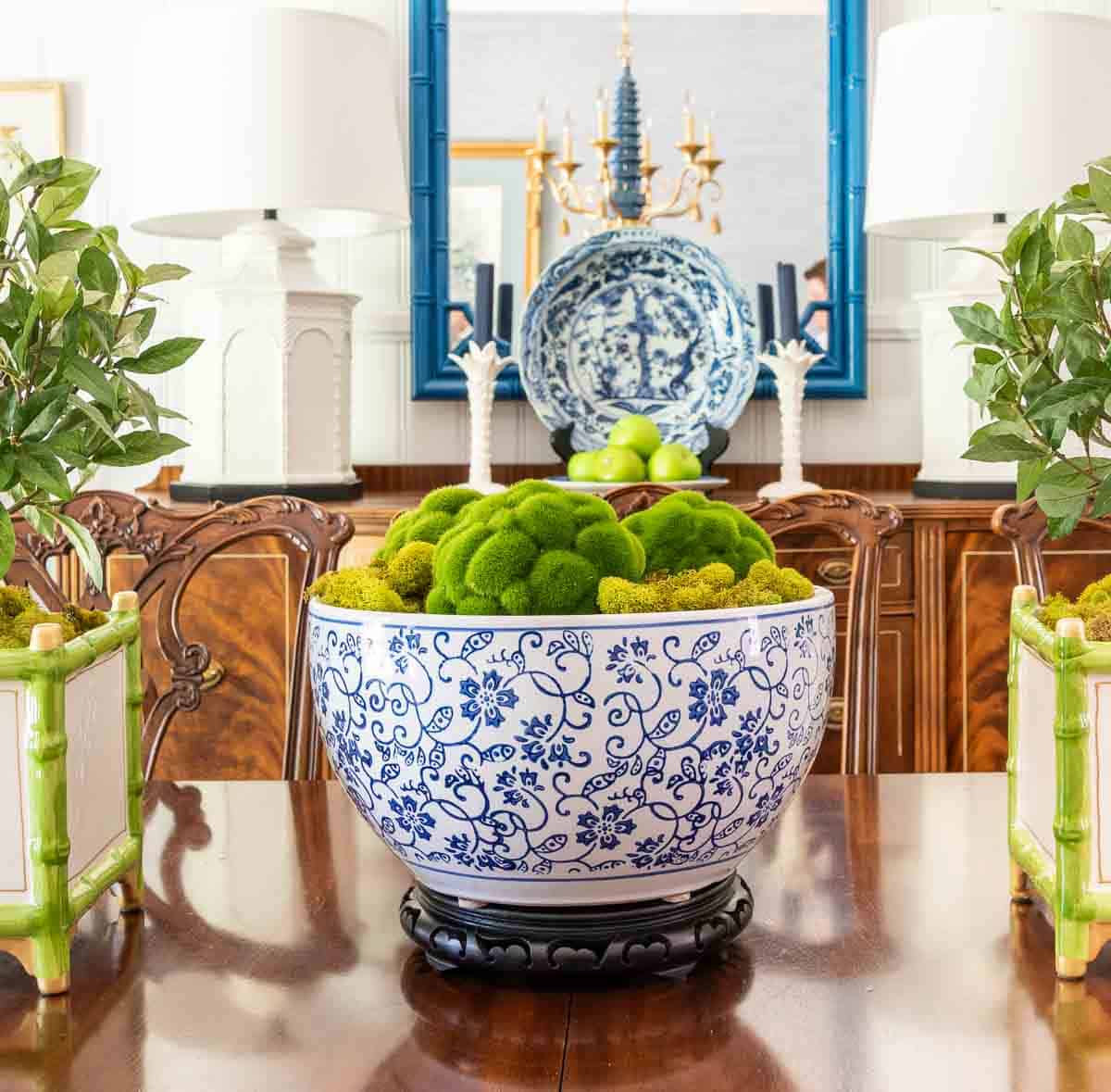 large blue and white bowl filled with moss and moss balls in a dining room table centerpiece