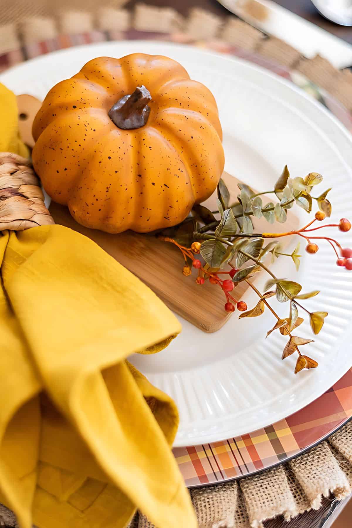 fall place setting with a plaid charger, white plate topped with a mini pumpkin