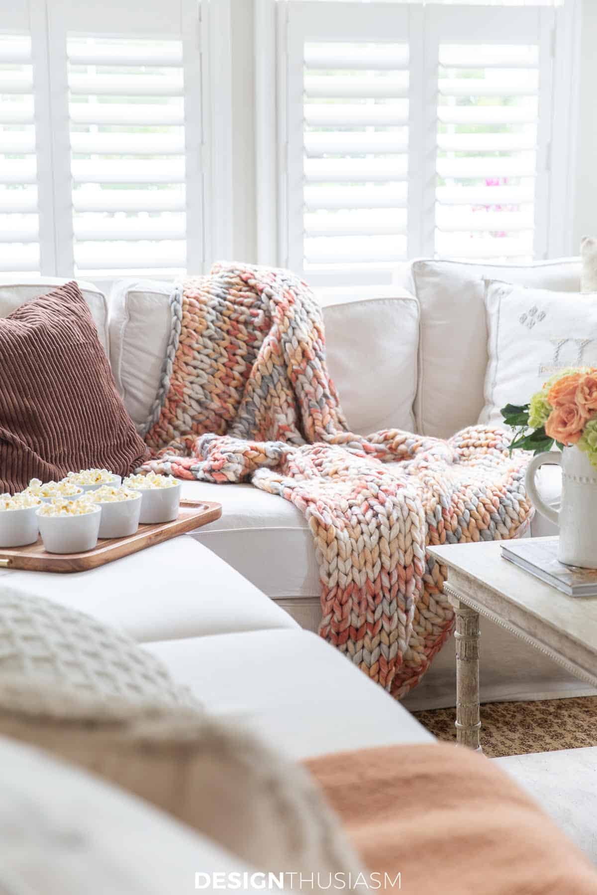 a white sectional sofa in front of window with plantation shutters