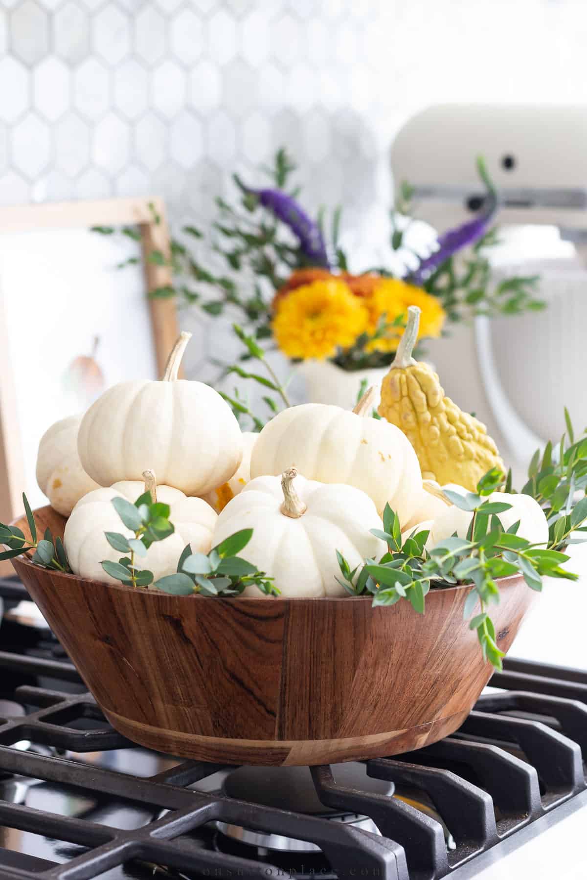 round wooden bowl filled with white mini pumpkins and greenery