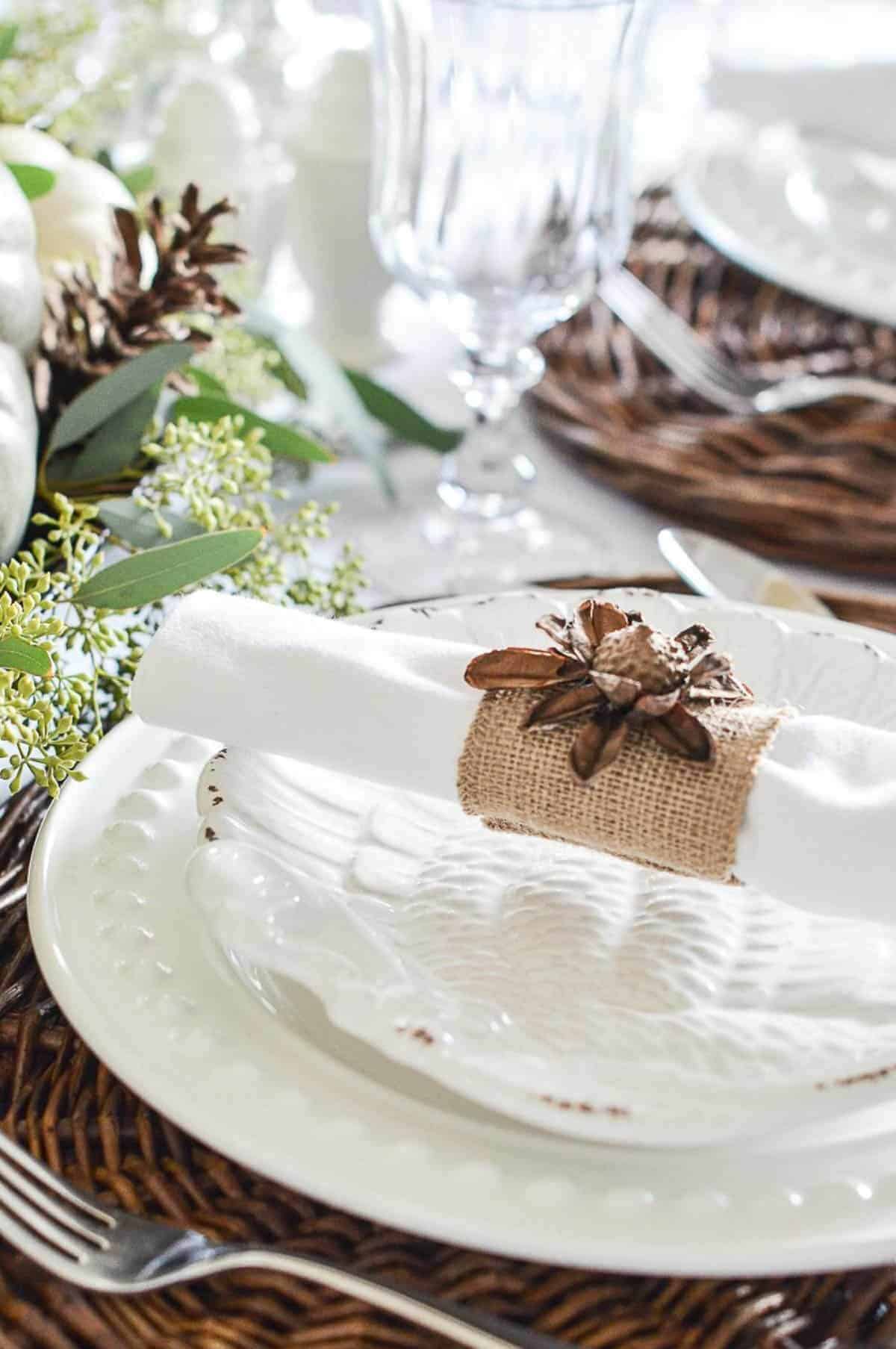 place setting with white dishes and a white napkin with a burlap napkin ring