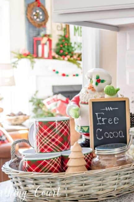 Christmas mugs next to a Santa figurine holding a chalkboard