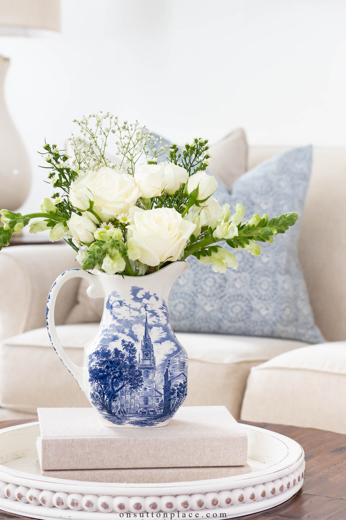 white flower arrangement in a blue and white pitcher on a coffee table