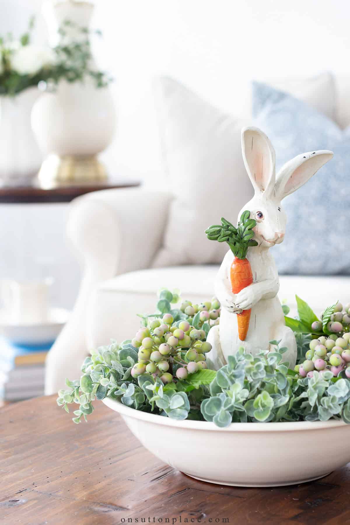 white ceramic bunny holding a carrot in a bowl of faux greenery and berries