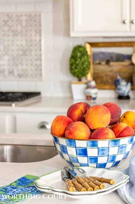 bowl of peaches in a blue and white checked bowl on a white kitchen counter