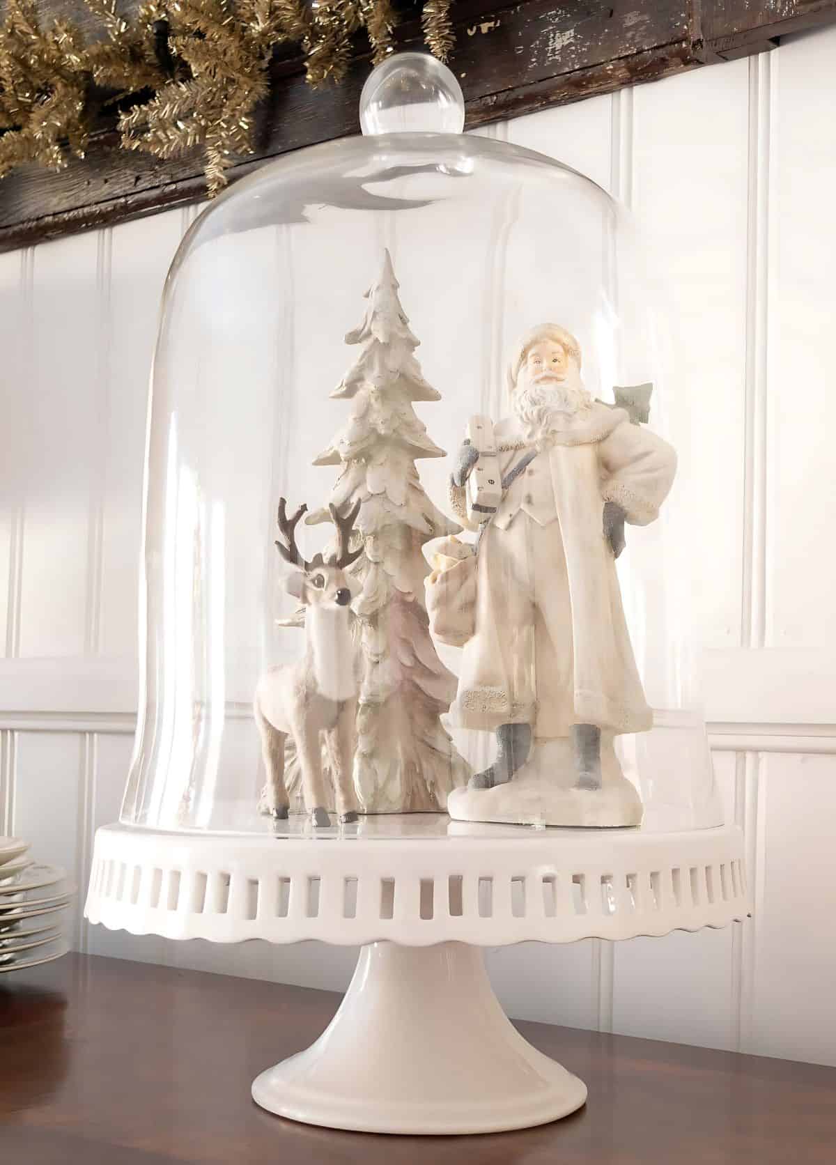 neutral Santa, deer, and frosty tree under a cloche on a white pedestal