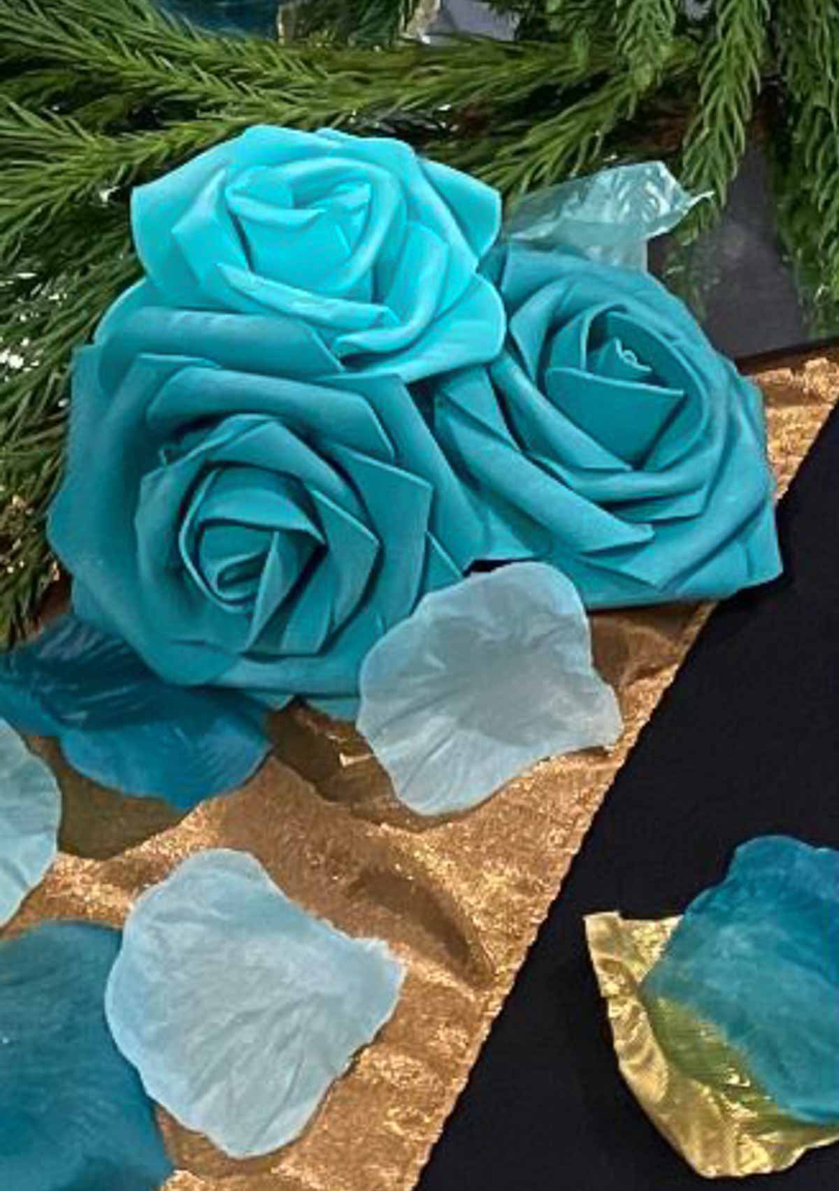 trio of turquoise roses on a gold table runner on a black tablecloth