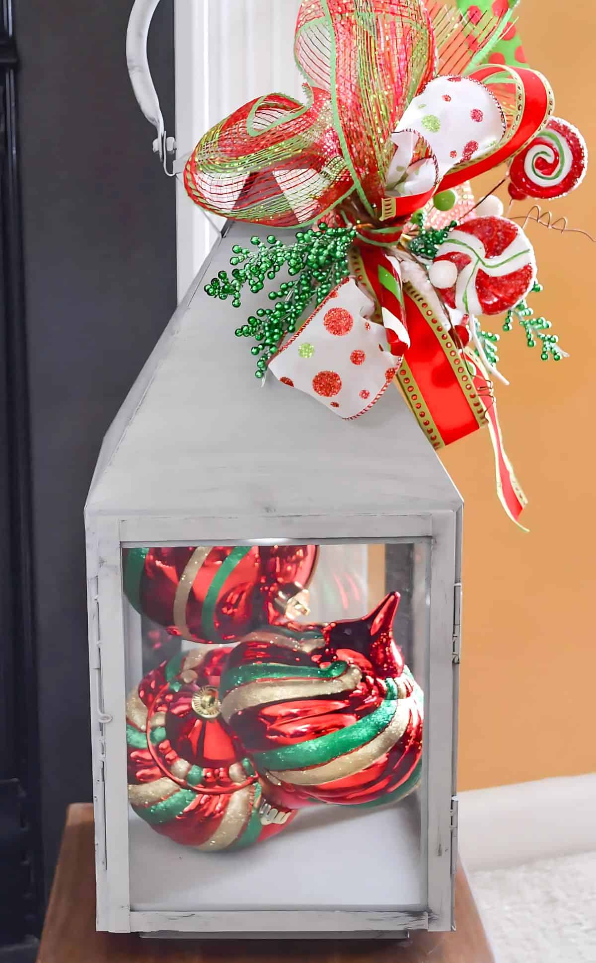 large lantern filled with red ornaments topped with a sparkly bow