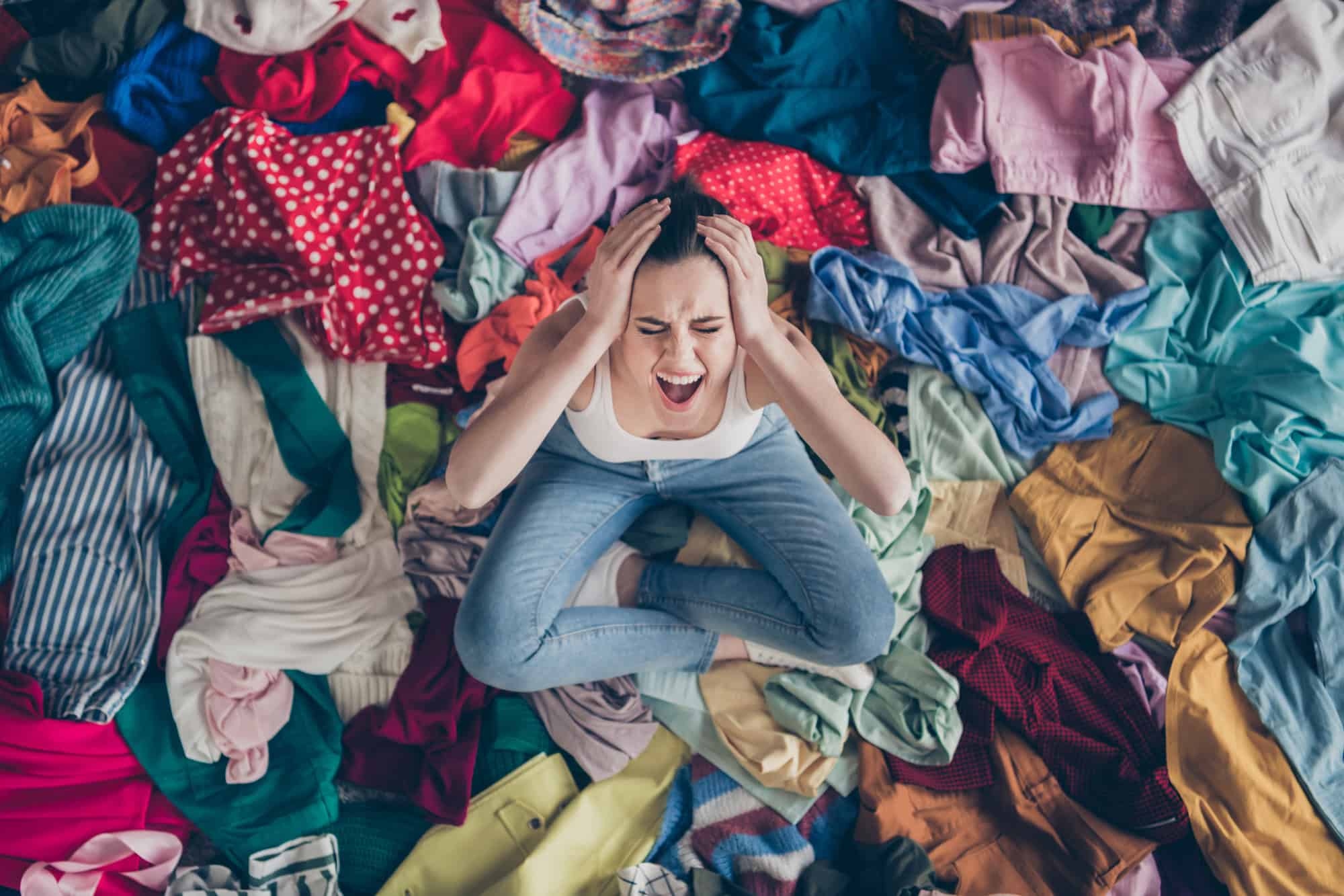 overwhelmed woman sitting in a pile of clothes on the floor