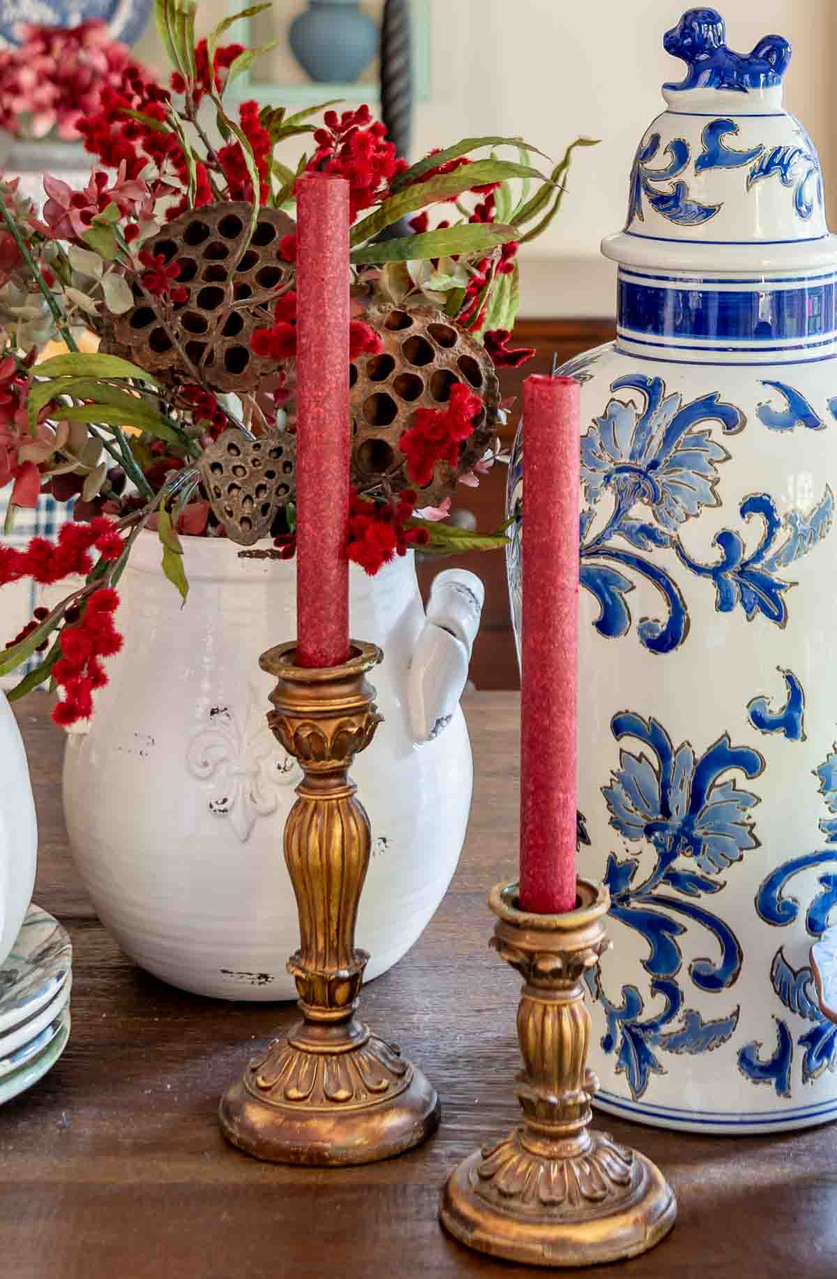 a diy fall table centerpiece using blue, white and burgundy colors, consisting of a large lidded urn, a floral arrangement, and a large white pumpkin on a stack of fall plates