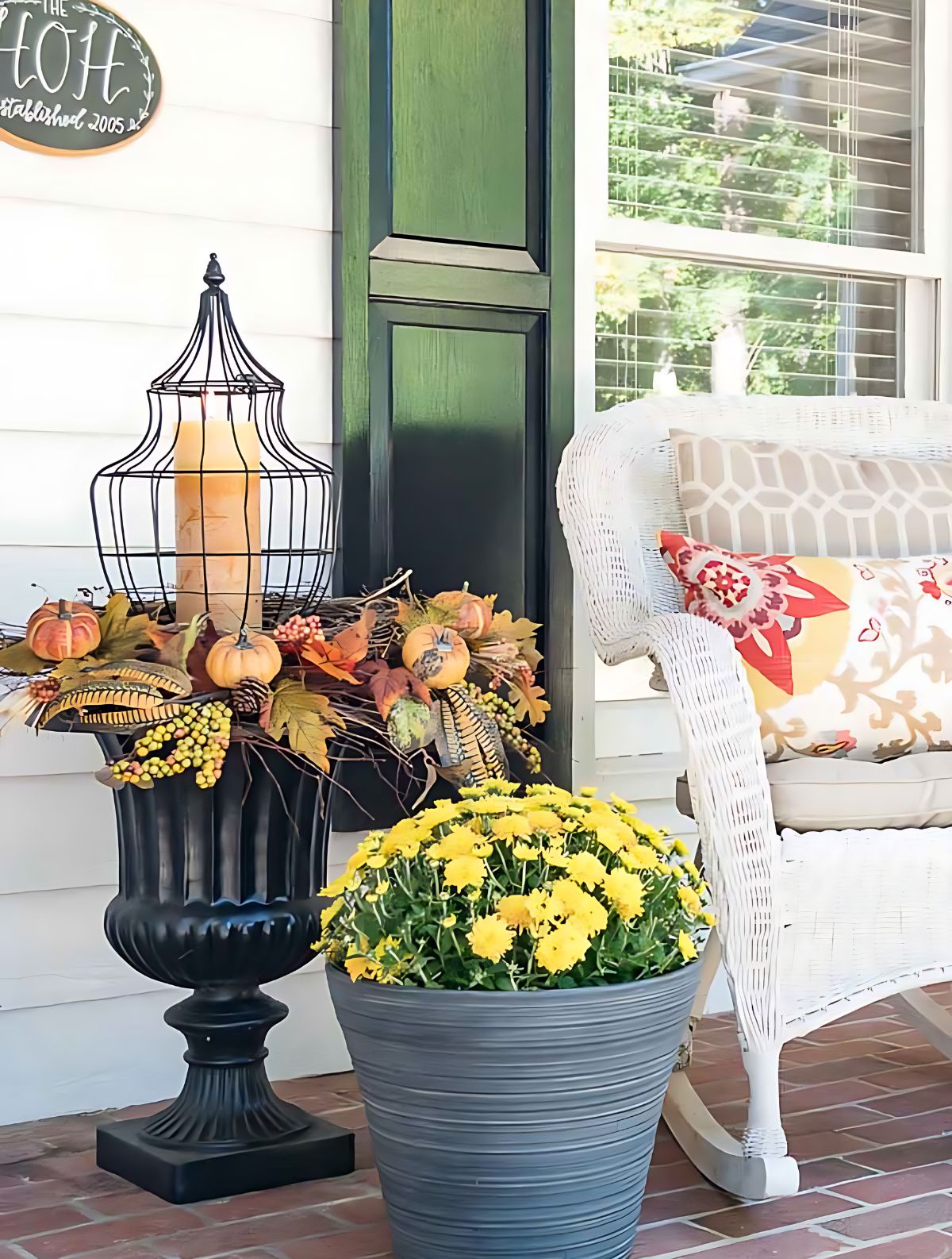 fall arrangement in a black urn with a tall lantern and candle in the center, filled in with fall-themed picks around the rim of the planter