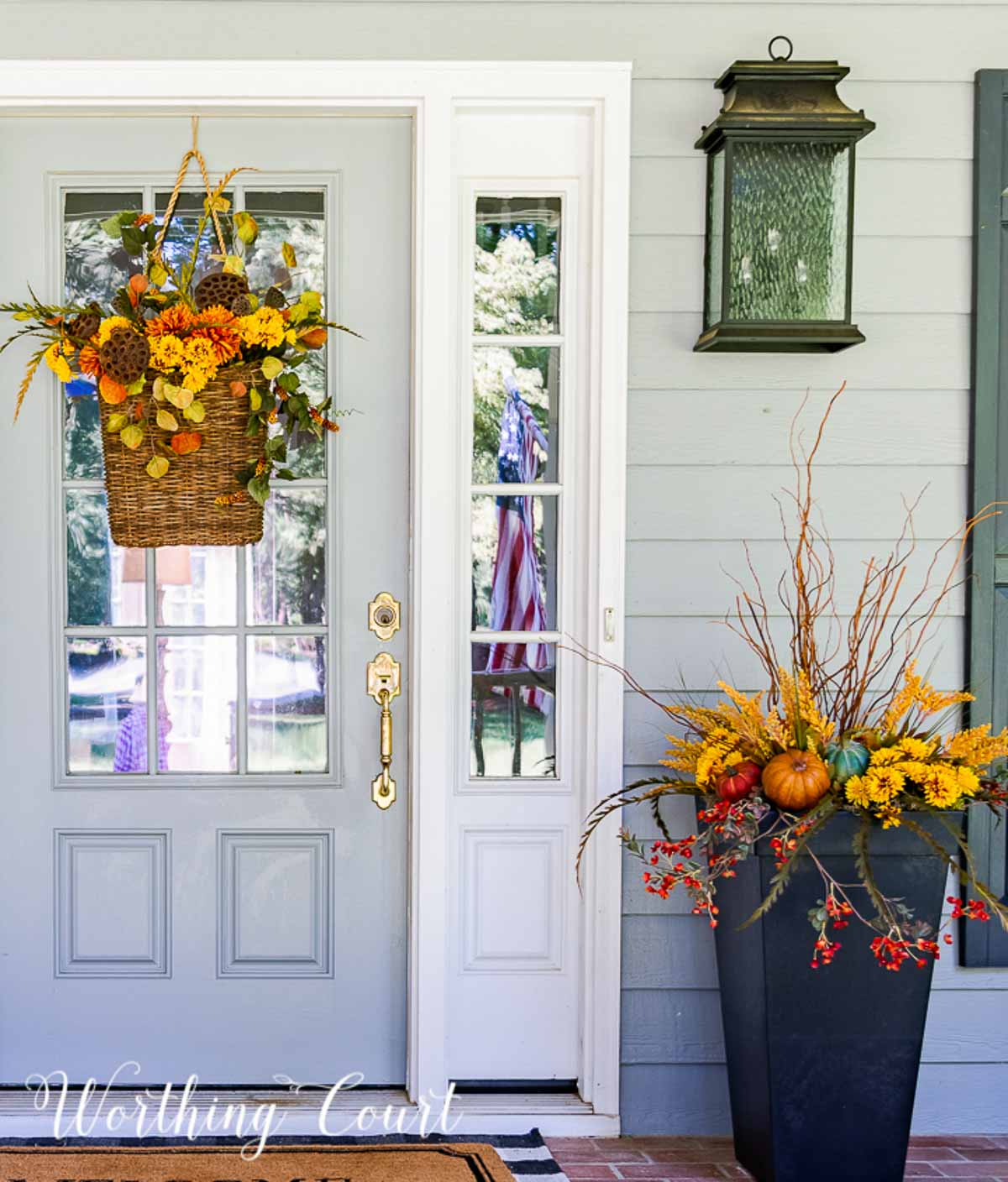 fall arrangement in a square planter beside a gray front door with a fall hanging basket arrangement for the wreath