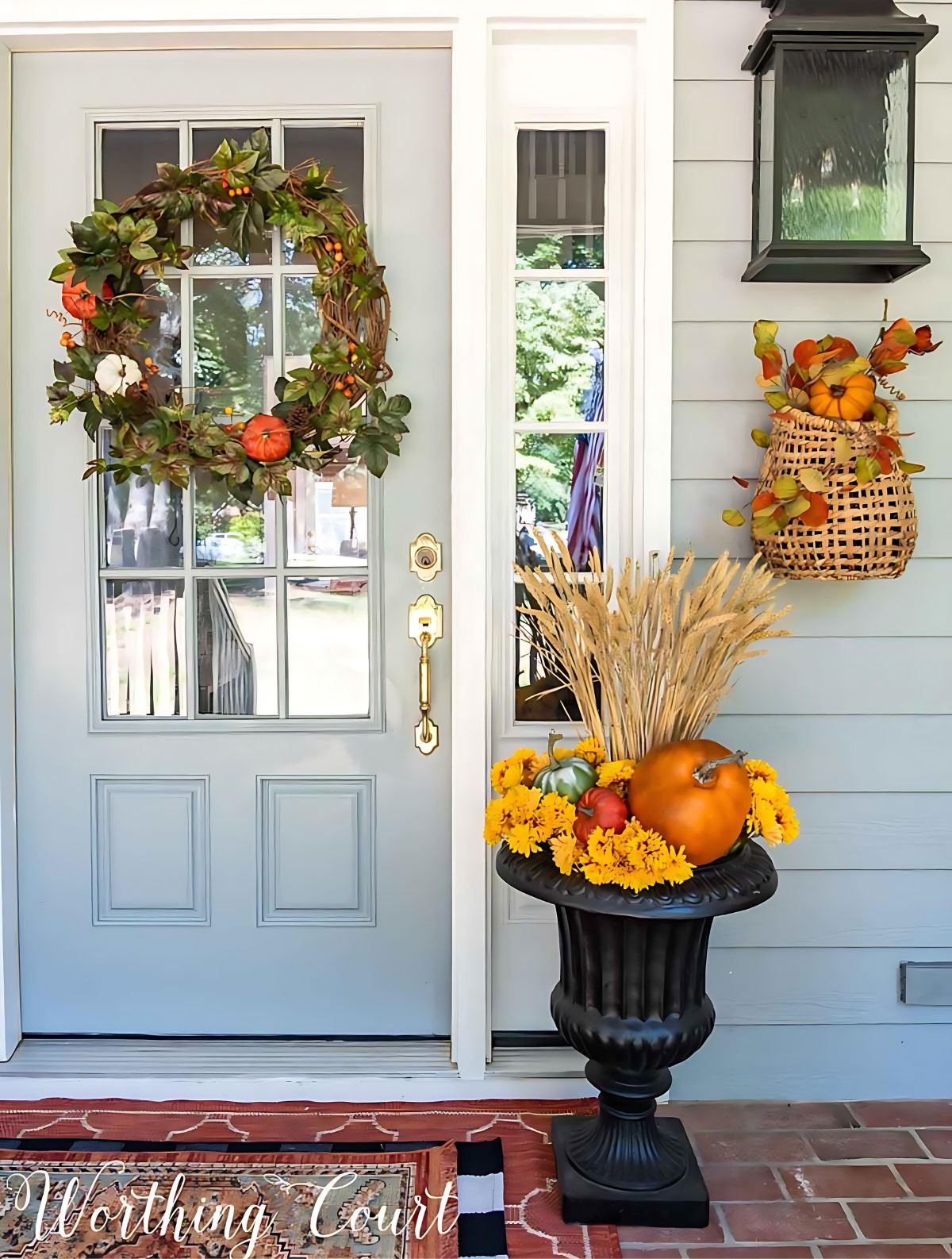 fall container and wreath on a front porch in front of a gray house using traditional fall colors and elements